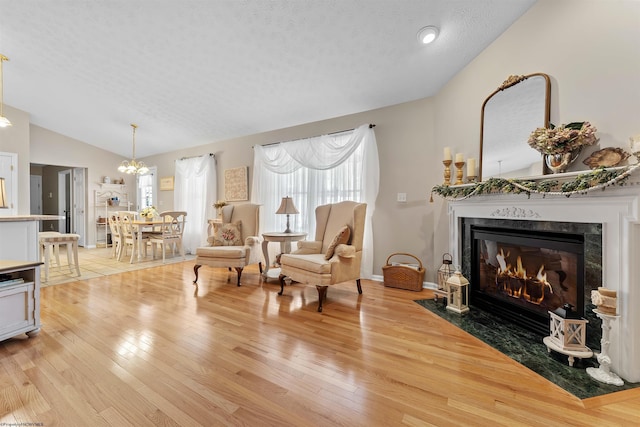 living area featuring a textured ceiling, light hardwood / wood-style flooring, a high end fireplace, and lofted ceiling