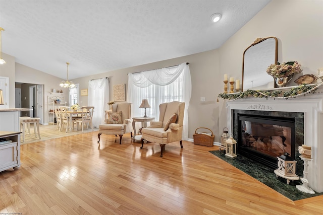 living area featuring a high end fireplace, a textured ceiling, light hardwood / wood-style flooring, and vaulted ceiling