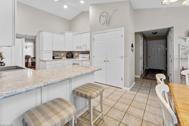 kitchen featuring a breakfast bar, white appliances, sink, kitchen peninsula, and white cabinetry