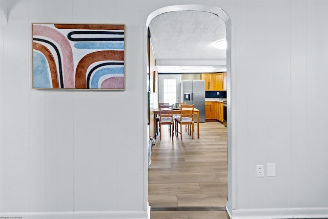 corridor with light wood-type flooring, a textured ceiling, and wooden walls