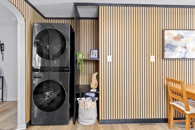 clothes washing area featuring a textured ceiling, wood-type flooring, and stacked washer / dryer