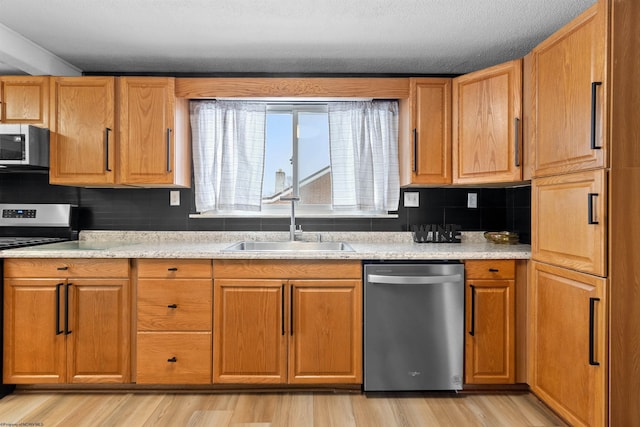 kitchen featuring sink, decorative backsplash, a textured ceiling, appliances with stainless steel finishes, and light hardwood / wood-style floors