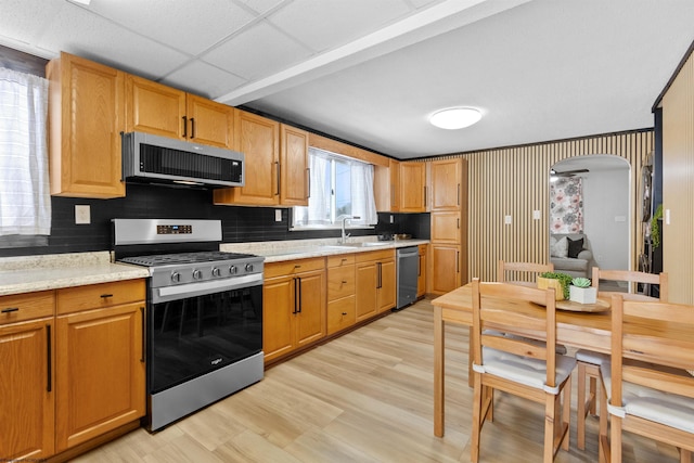 kitchen with a paneled ceiling, sink, light hardwood / wood-style flooring, light stone countertops, and appliances with stainless steel finishes