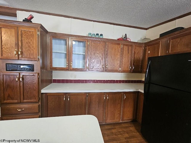 kitchen with black refrigerator, ornamental molding, a textured ceiling, and dark wood-type flooring