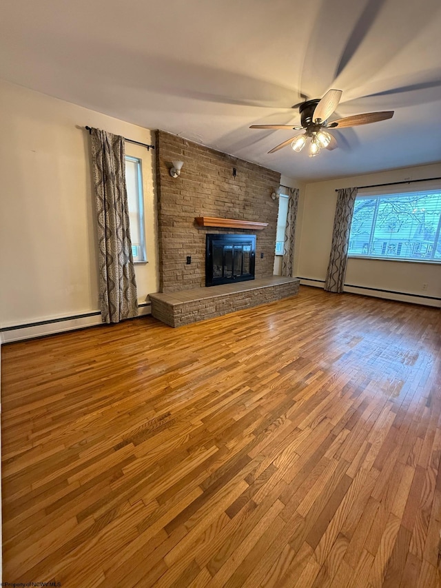 unfurnished living room with a fireplace, light wood-type flooring, ceiling fan, and a baseboard heating unit