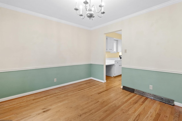 spare room with a notable chandelier, light wood-type flooring, and ornamental molding