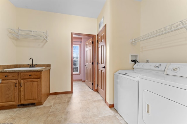 clothes washing area with washing machine and dryer, sink, and cabinets