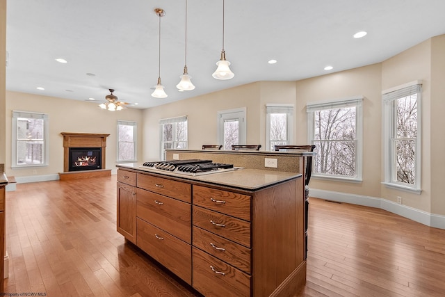 kitchen featuring hanging light fixtures, a center island, a healthy amount of sunlight, stainless steel gas stovetop, and light wood-type flooring