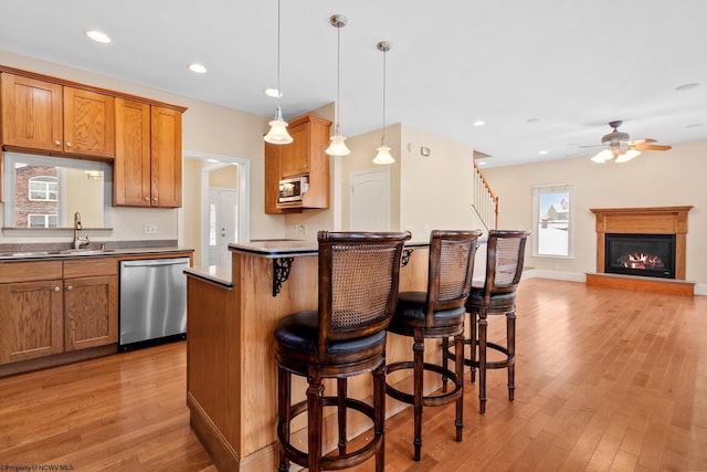 kitchen with pendant lighting, sink, a kitchen breakfast bar, stainless steel appliances, and light wood-type flooring