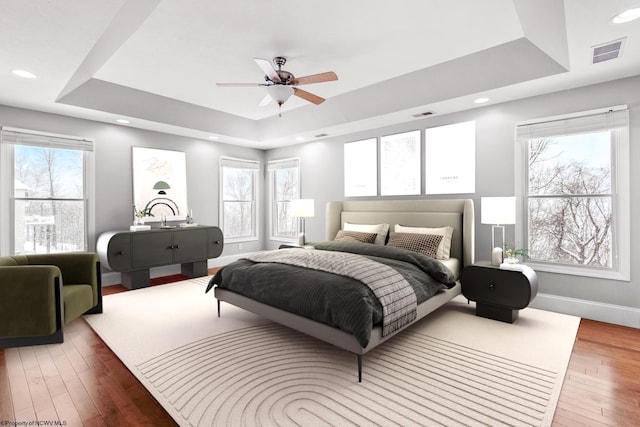 bedroom featuring a raised ceiling, hardwood / wood-style floors, and multiple windows