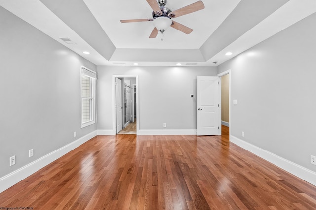 empty room with ceiling fan, wood-type flooring, and a tray ceiling