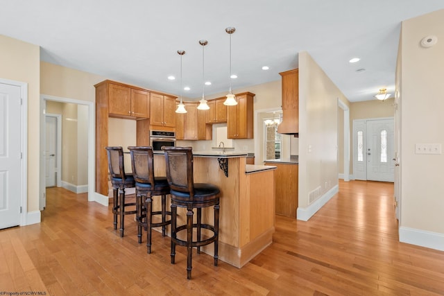 kitchen featuring pendant lighting, a kitchen bar, a center island, stainless steel oven, and light wood-type flooring