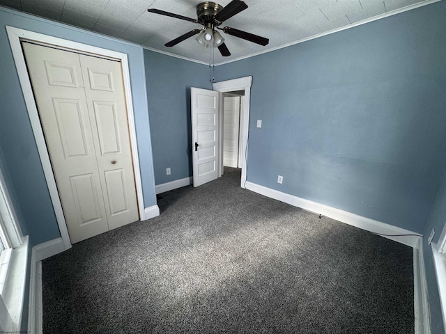 unfurnished bedroom featuring dark colored carpet, a closet, ceiling fan, and crown molding