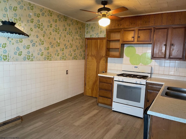 kitchen with ceiling fan, white gas stove, sink, crown molding, and wood-type flooring