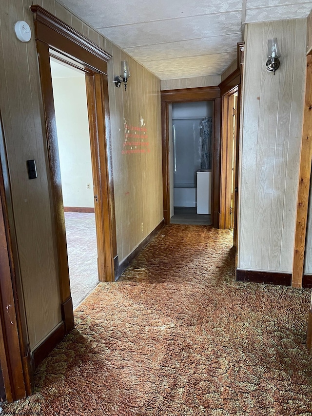 hall with dark colored carpet and wood walls