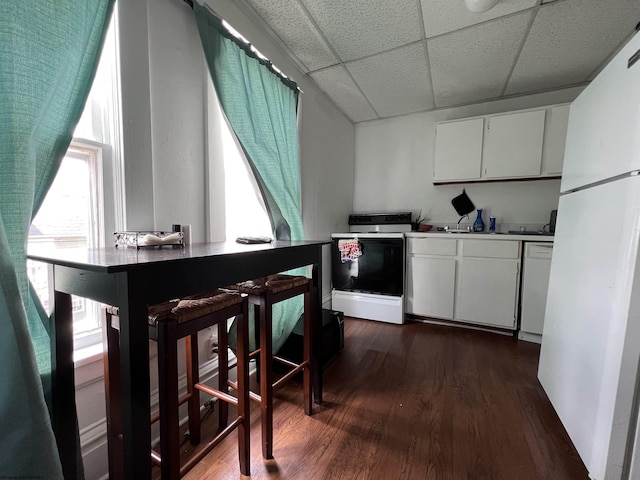 kitchen with white cabinetry, a wealth of natural light, dark wood-type flooring, white appliances, and a paneled ceiling