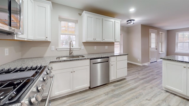 kitchen with light stone countertops, appliances with stainless steel finishes, white cabinetry, and sink