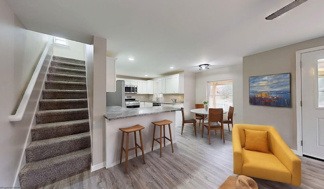 kitchen featuring dark stone counters, white cabinets, light hardwood / wood-style floors, kitchen peninsula, and stainless steel appliances