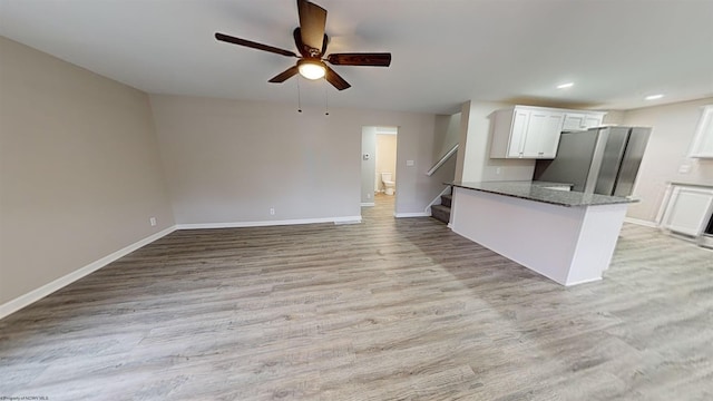 kitchen featuring stainless steel refrigerator, white cabinetry, ceiling fan, kitchen peninsula, and dark stone counters