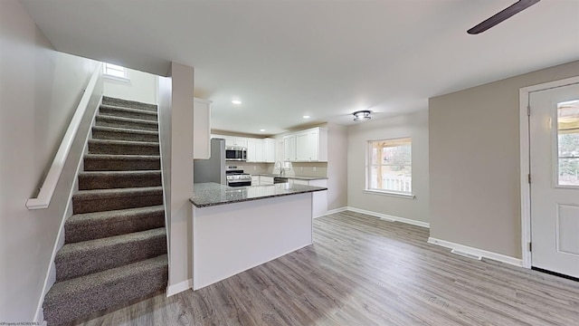 kitchen with kitchen peninsula, appliances with stainless steel finishes, dark stone countertops, white cabinets, and light hardwood / wood-style floors