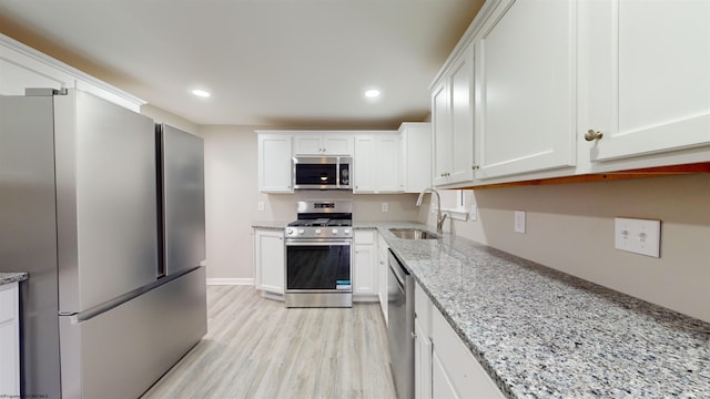 kitchen with white cabinets, appliances with stainless steel finishes, light stone counters, and sink