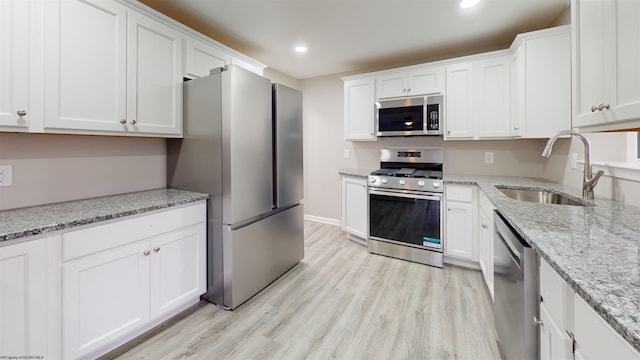 kitchen with white cabinetry, sink, stainless steel appliances, light stone counters, and light hardwood / wood-style flooring