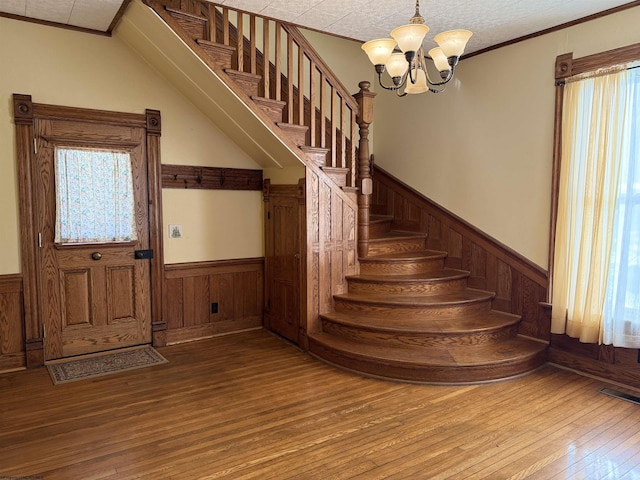 stairs with crown molding, wood-type flooring, and an inviting chandelier