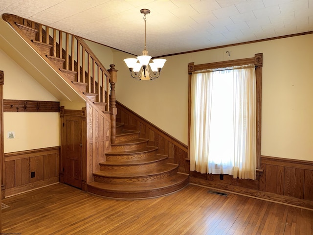 stairs with a chandelier, wood-type flooring, and ornamental molding