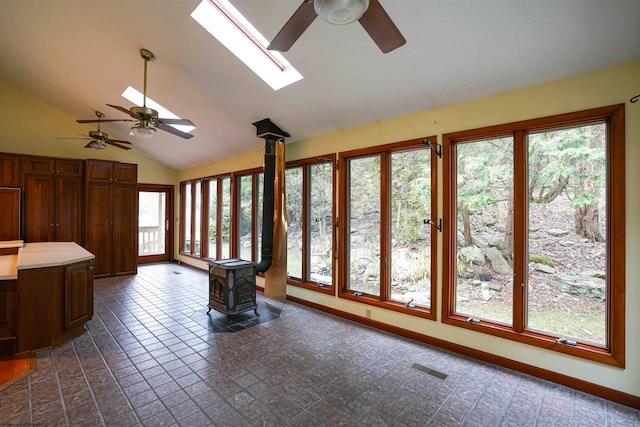 interior space featuring ceiling fan, a wood stove, and lofted ceiling with skylight