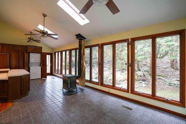 unfurnished sunroom featuring lofted ceiling with skylight, ceiling fan, a wood stove, and stacked washer and clothes dryer