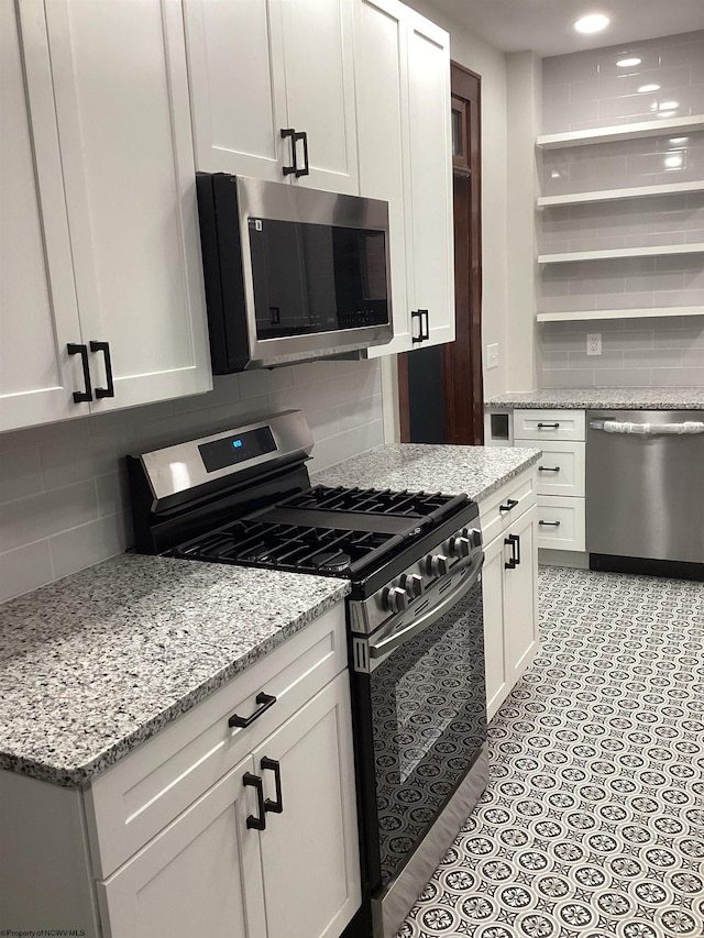 kitchen with white cabinets, appliances with stainless steel finishes, tasteful backsplash, and light stone counters