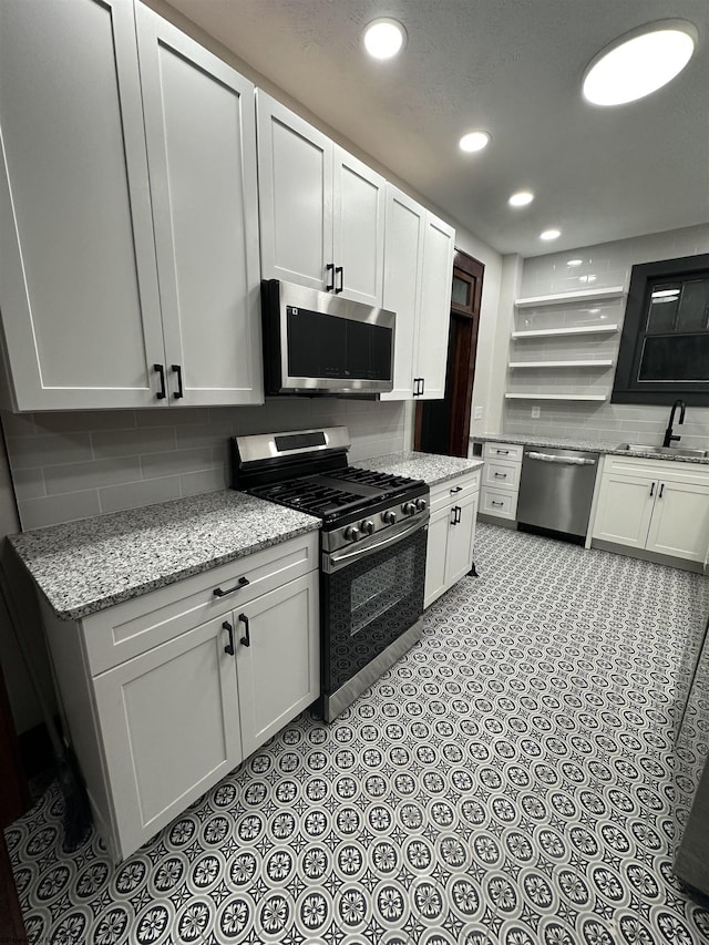 kitchen with white cabinets, appliances with stainless steel finishes, light stone counters, and sink