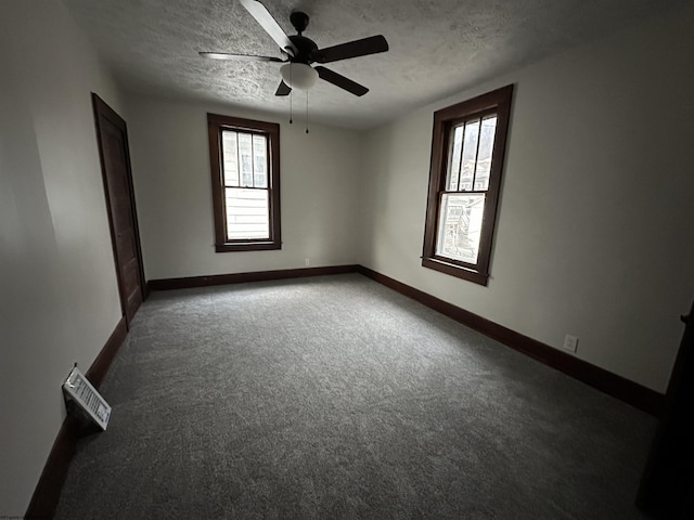 empty room featuring ceiling fan, plenty of natural light, a textured ceiling, and dark colored carpet