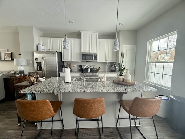 kitchen with light stone countertops, appliances with stainless steel finishes, decorative backsplash, decorative light fixtures, and white cabinets