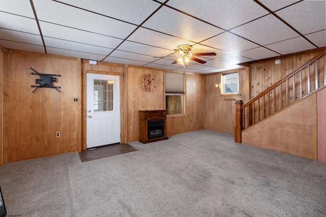 unfurnished living room with a wealth of natural light, ceiling fan, wooden walls, and carpet