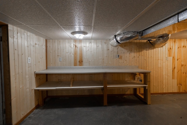 basement featuring a drop ceiling and wooden walls