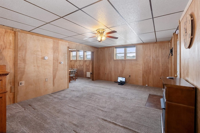 unfurnished room with carpet flooring, a drop ceiling, ceiling fan, and wooden walls