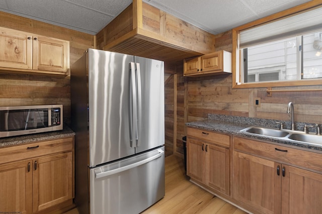 kitchen with sink, stainless steel appliances, wooden walls, and light hardwood / wood-style flooring