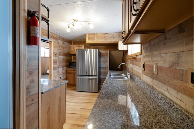 kitchen featuring appliances with stainless steel finishes, sink, dark stone countertops, light hardwood / wood-style floors, and wood walls