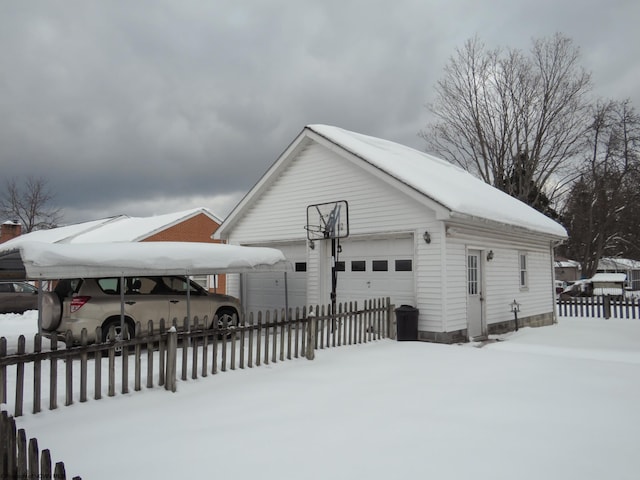 view of snowy exterior featuring a carport, a garage, and an outdoor structure