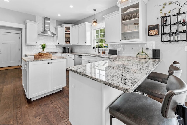 kitchen with sink, white cabinetry, wall chimney exhaust hood, kitchen peninsula, and pendant lighting