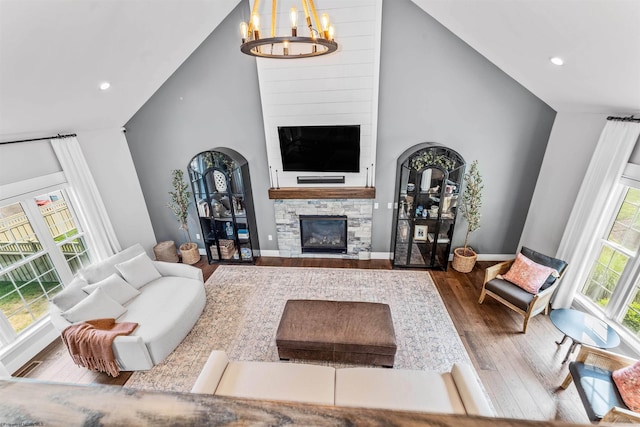 living room with a towering ceiling, a chandelier, hardwood / wood-style flooring, and a stone fireplace