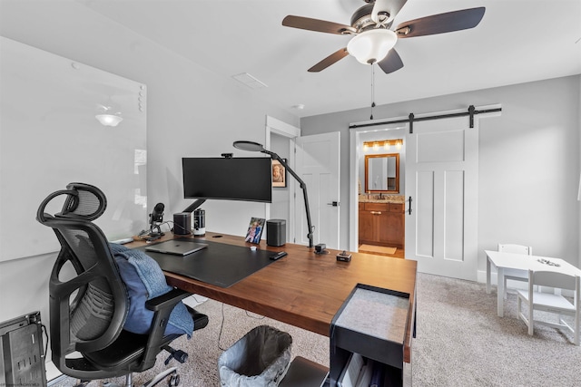 carpeted home office featuring ceiling fan and a barn door