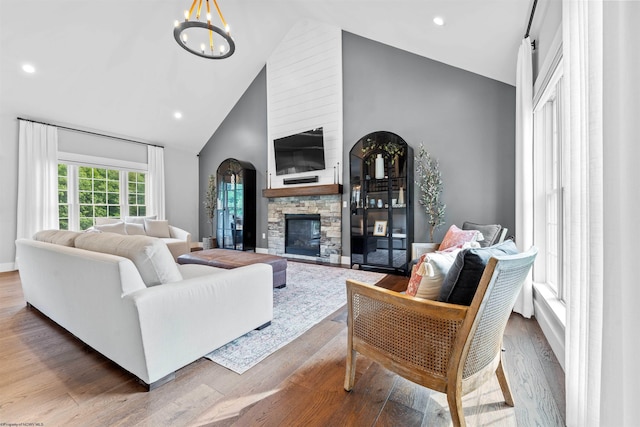 living room with high vaulted ceiling, a chandelier, wood-type flooring, and a stone fireplace