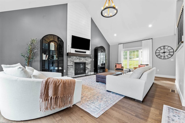 living room with high vaulted ceiling, dark hardwood / wood-style flooring, a notable chandelier, and a stone fireplace