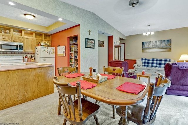 dining space with ceiling fan with notable chandelier, vaulted ceiling, and light colored carpet