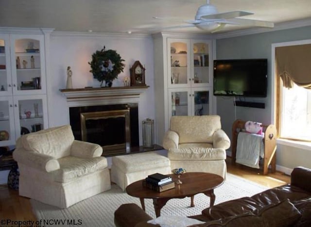 living room featuring ceiling fan, a glass covered fireplace, wood finished floors, and crown molding