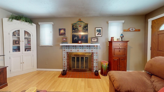 living room with a brick fireplace, a textured ceiling, a wealth of natural light, and light hardwood / wood-style floors