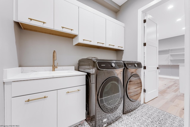 laundry room featuring sink, washer and dryer, light wood-type flooring, and cabinets