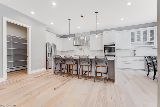 kitchen featuring decorative light fixtures, a center island with sink, stainless steel fridge with ice dispenser, a baseboard heating unit, and white cabinets